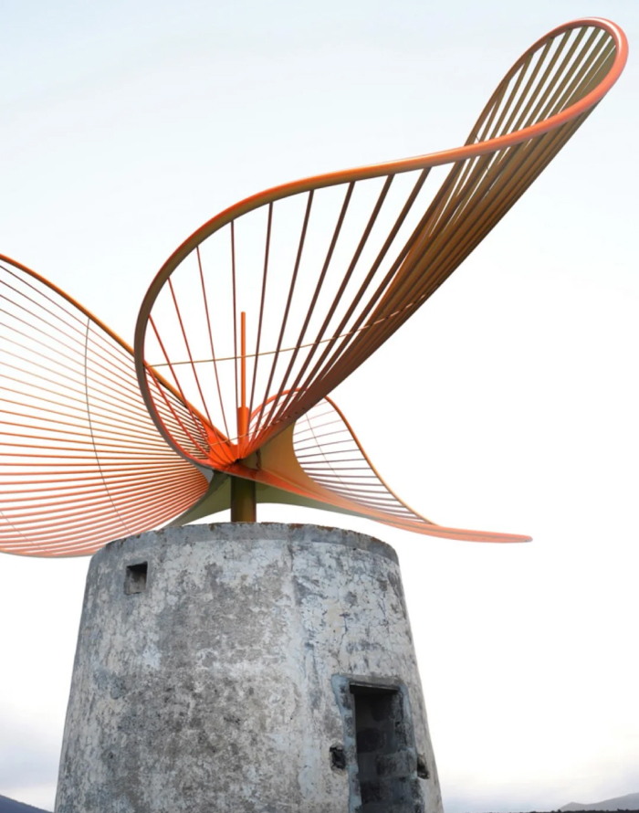 Modern architecture design: A contemporary orange abstract sculpture atop an old stone structure, set against a clear sky.
