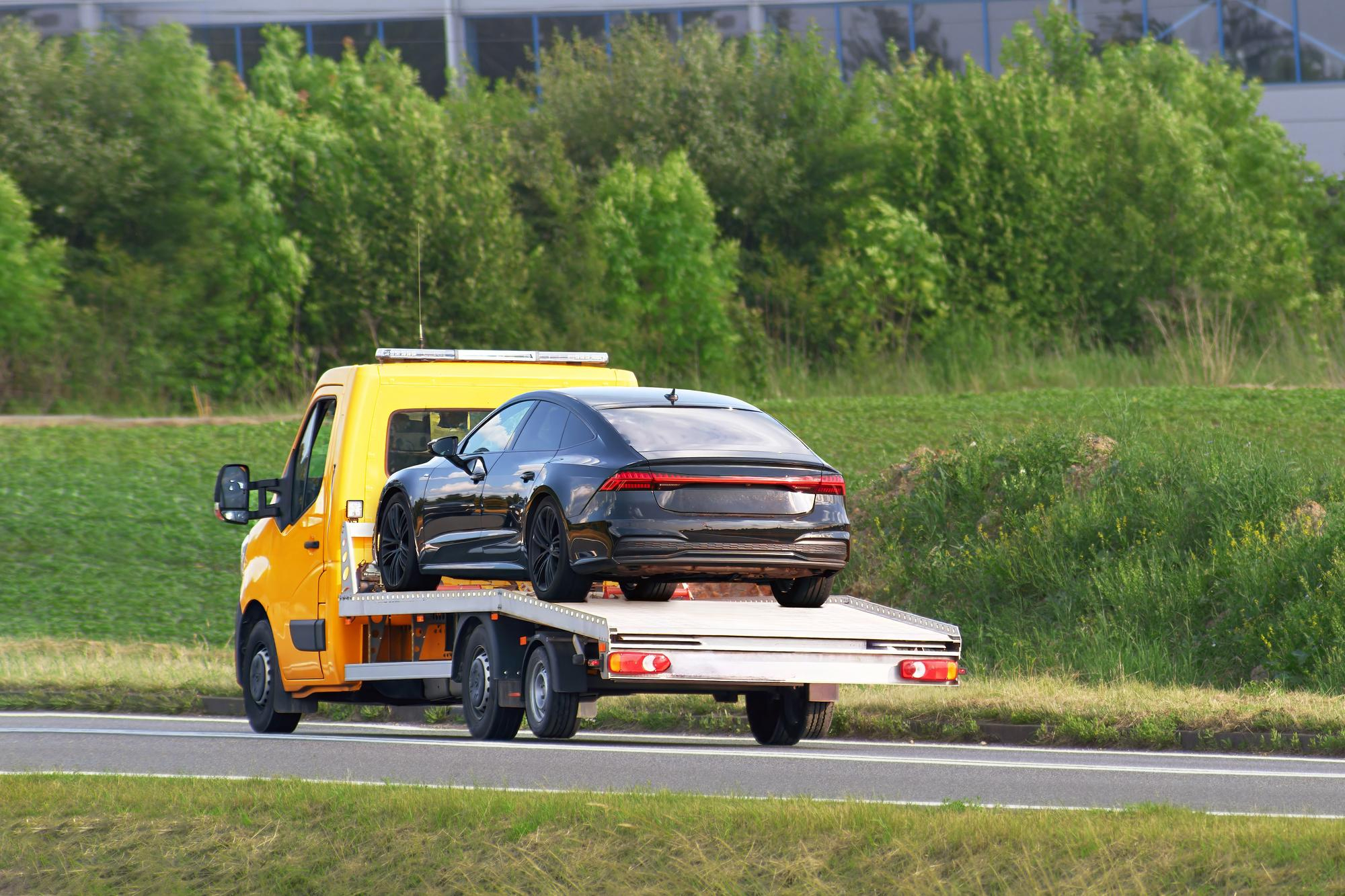 A black car being towed on a yellow tow truck, symbolizing the beloved BMW taken away in a parking war.