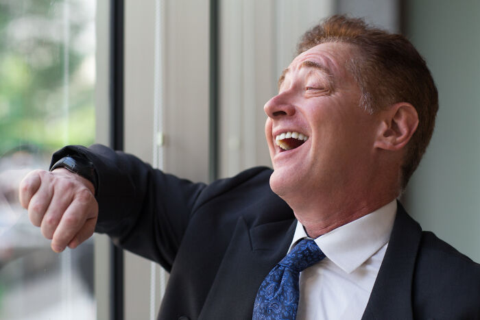 A happy worker laughing by a window, finding humor in corporate buzzwords and practices.
