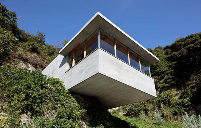Modern architecture design: A cantilevered concrete house nestled into a green hillside, featuring a bold, minimalist design.