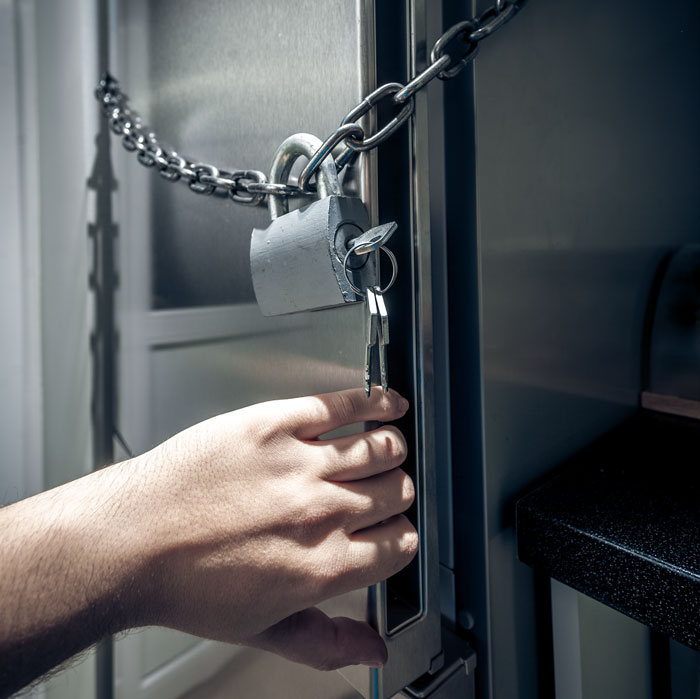 A hand holding keys to a lock and chain securing a fridge, symbolizing a moocher situation.