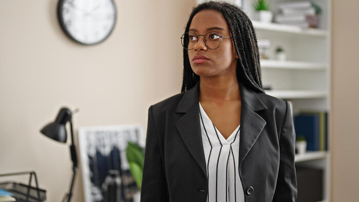 A woman with glasses and braids, appearing thoughtful or frustrated by corporate buzzwords.