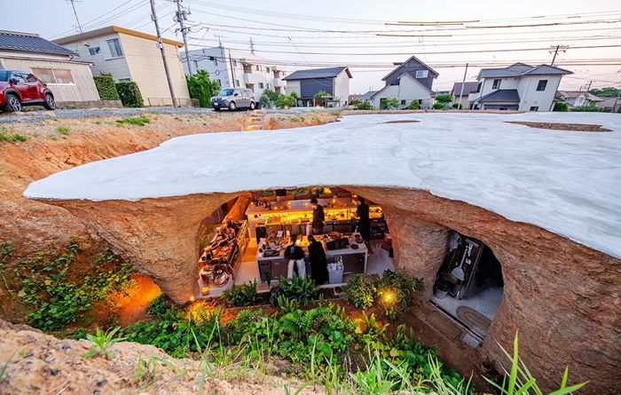 Amazing modern architecture design of a unique underground cafe with a nature-inspired roof, surrounded by green plants.