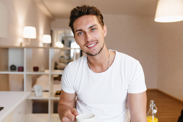 A smiling man in a white t-shirt holding a coffee cup, representing a student worker's career.