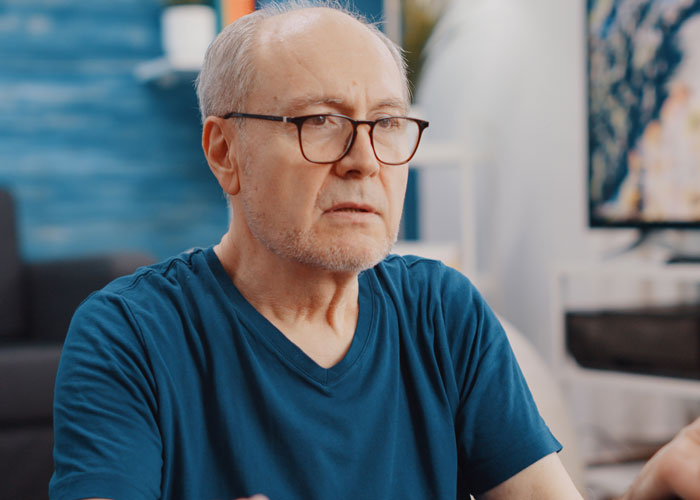 A man with glasses and a blue t-shirt, looking stern, representing the MIL turning pregnancy into a competition with no sympathy. A man with glasses and a blue t-shirt, looking stern, representing the MIL turning pregnancy into a competition with no sympathy.
