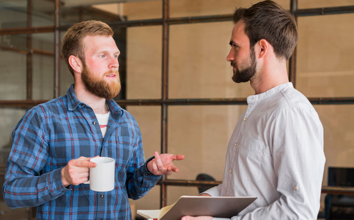 Two male coworkers talking, one holding a mug. The image relates to a job ending after rejection. Two male coworkers talking, one holding a mug. The image relates to a job ending after rejection.