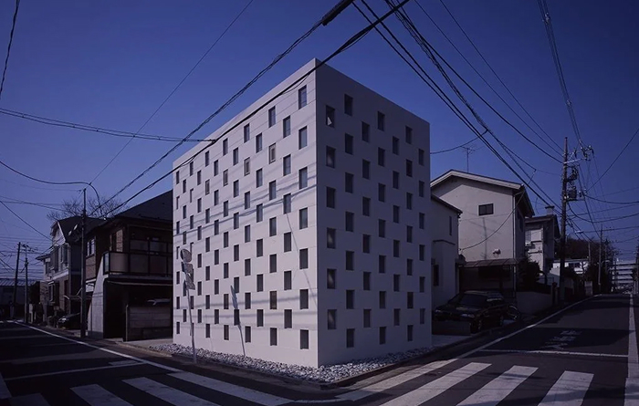 Modern architecture design: A minimalist white building with many small windows, surrounded by power lines in an urban setting.