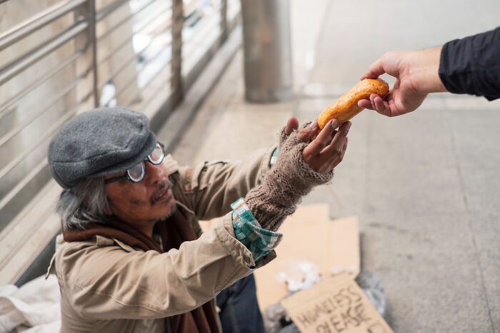 A person offering bread to a homeless man, illustrating one of the dumbest reasons people got fired.