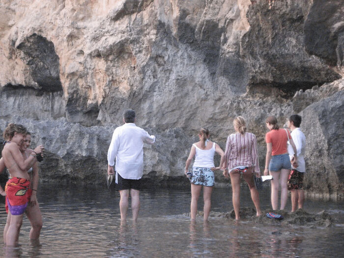 A group of people standing in shallow water near a rock face, capturing a moment someone asked a celebrity for a photo.