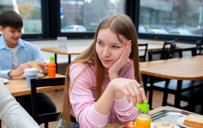 A teen girl with long blonde hair, looking thoughtful while sitting at a table with a tray of food, demonstrating what happens if she's forced to eat what she doesn't want to. A teen girl with long blonde hair, looking thoughtful while sitting at a table with a tray of food, demonstrating what happens if she's forced to eat what she doesn't want to.