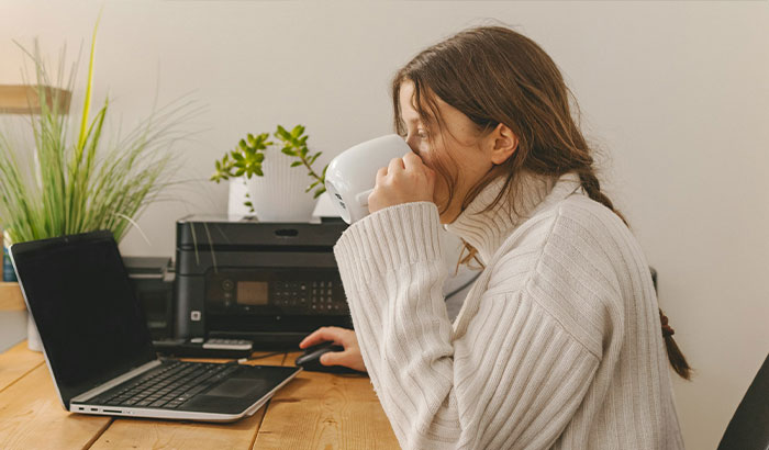 A woman upset about football fiancé response, drinking from a mug while working on a laptop at a wooden desk. A woman upset about football fiancé response, drinking from a mug while working on a laptop at a wooden desk.
