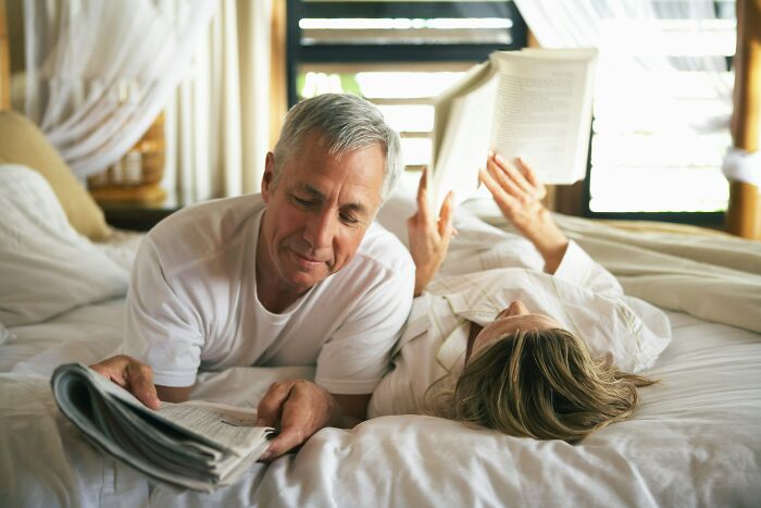 An older man and woman reading in bed, representing an age-gap relationship.