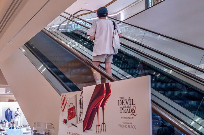 A person on an escalator walks past a large red high heel advertisement, an unbelievable street coincidence.