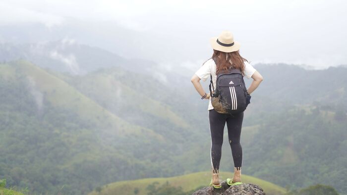 A woman with a backpack and hat looks out over green mountains, contemplating dating scenarios and red, green, beige flags.