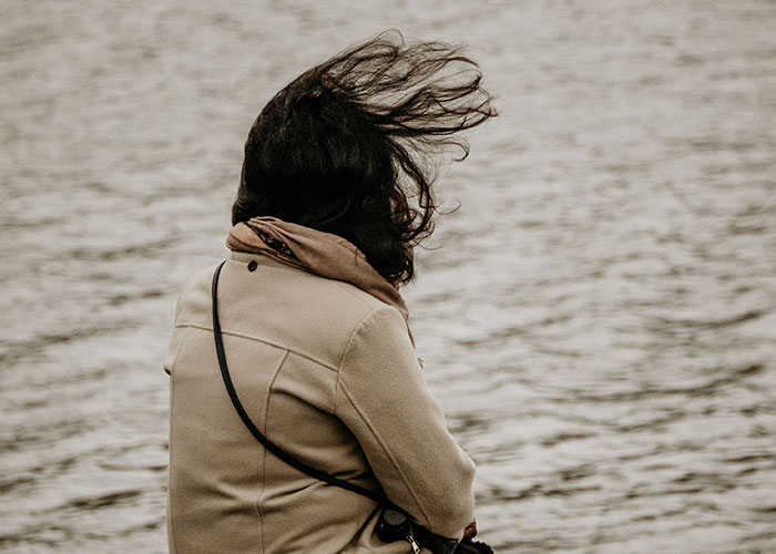 A person looking out at water, hair blowing in the wind, symbolizing loneliness and birthday sadness.