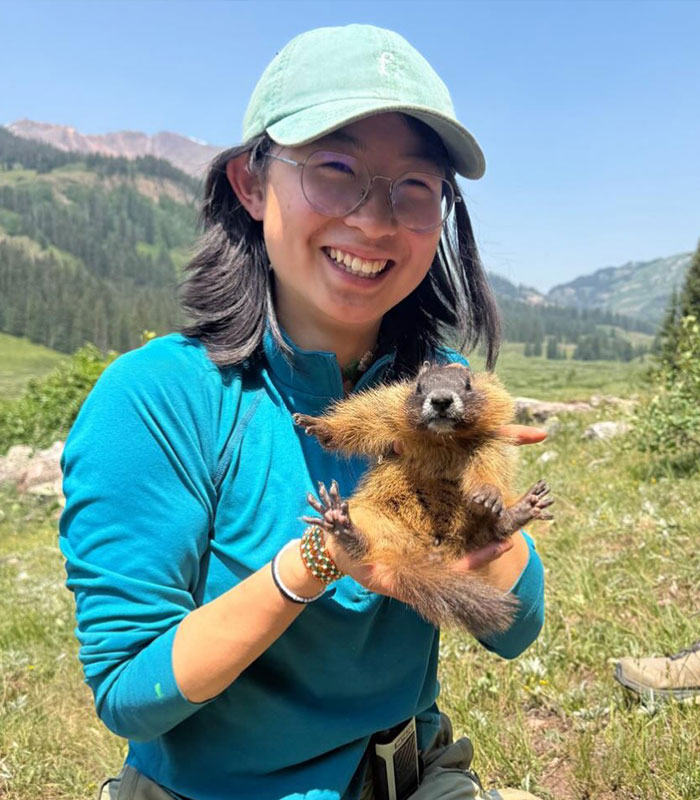 Smiling professor holding a marmot in a scenic outdoor setting, part of funding marmot studies. Smiling professor holding a marmot in a scenic outdoor setting, part of funding marmot studies.