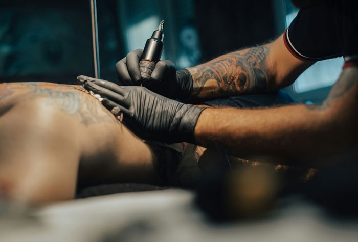A close-up of a tattoo artist working on a persons back, reflecting personal choices of men with partners.