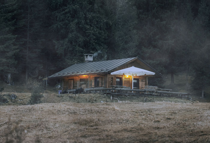A rustic cabin nestled in dark woods, symbolizing the mom's unconsulted travel plans that backfired.