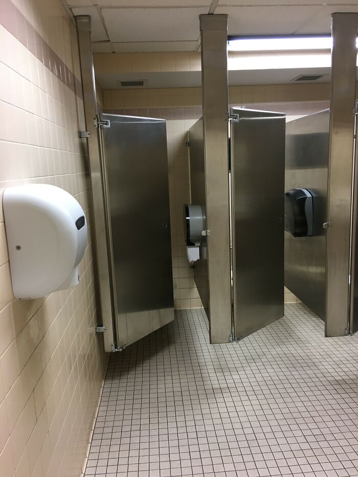 An empty public restroom with metal stalls, hinting at potential public horror stories.