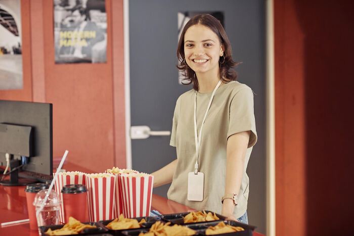 A smiling cinema worker stands behind a counter with popcorn, considering dumb reasons people got fired.