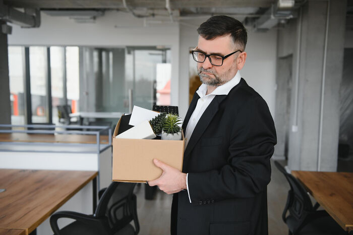 A man carries a box of his belongings, looking sad after being fired.
