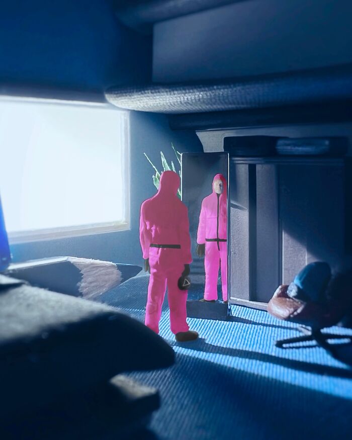 A tiny diorama set on an office desk by artist Derrick Lin, featuring two figures in pink jumpsuits looking into a mirror.