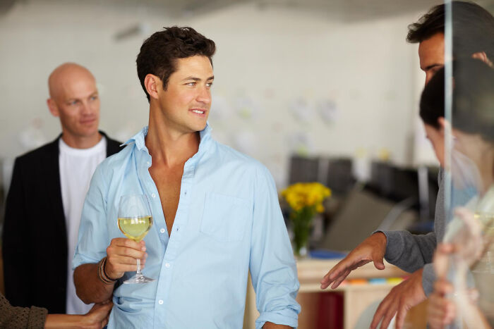A man at a social gathering holding a glass of wine, illustrating jobs guys have that make women swipe left.