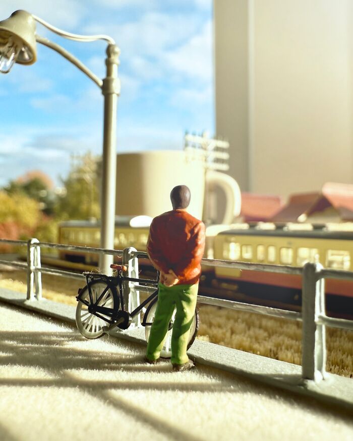 Derrick Lin creates a diorama set with a figure and bicycle watching a train pass by, a miniature office desk scene.