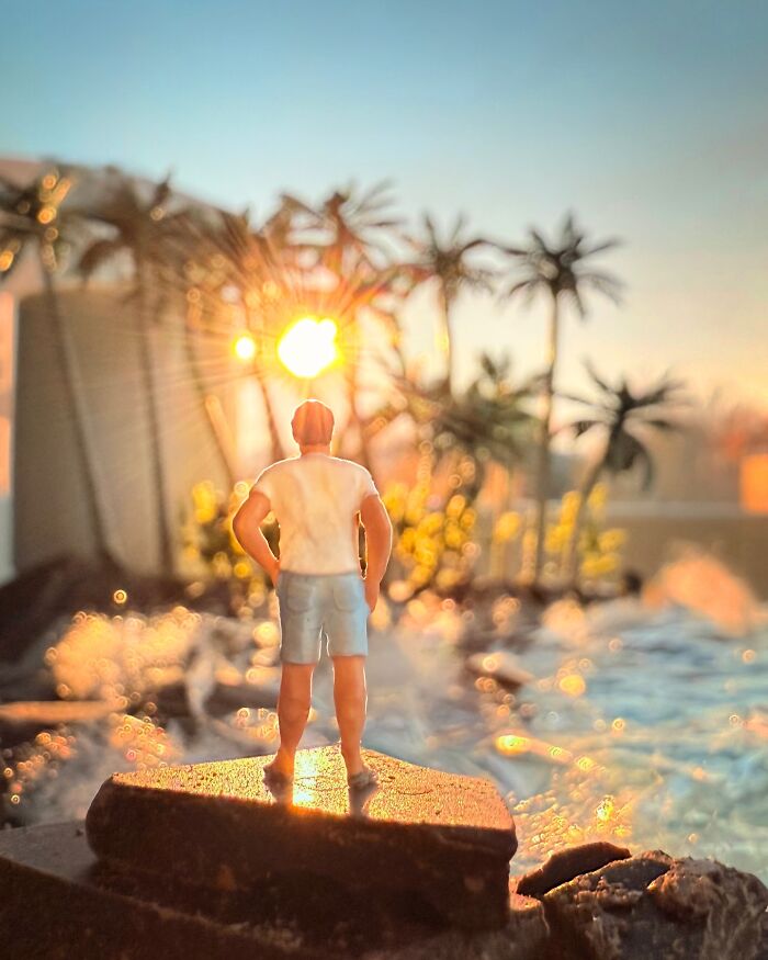 An intricate diorama set by Derrick Lin shows a figure on rocks overlooking a sunny, miniature ocean scene with palm trees.