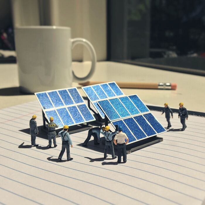 Artist Derrick Lin's intricate diorama set on an office desk, featuring tiny workers installing miniature solar panels.