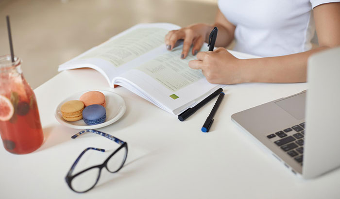 A woman studying at a table with a laptop, book, drink, and macarons, representing a new beginning after leaving her fiancé. A woman studying at a table with a laptop, book, drink, and macarons, representing a new beginning after leaving her fiancé.