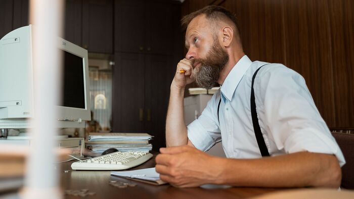 A thoughtful man at a desk, contemplating if he is in the wrong for not wearing his boyfriend's gift.