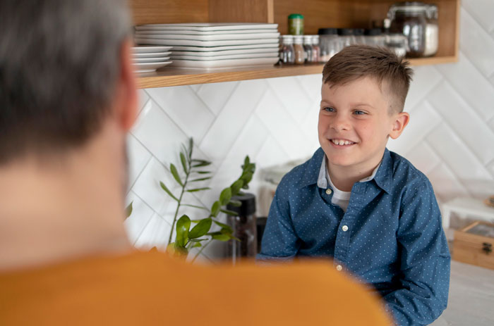 A young boy in a blue shirt smiling, looking at an adult in the foreground, showing a clever comeback.