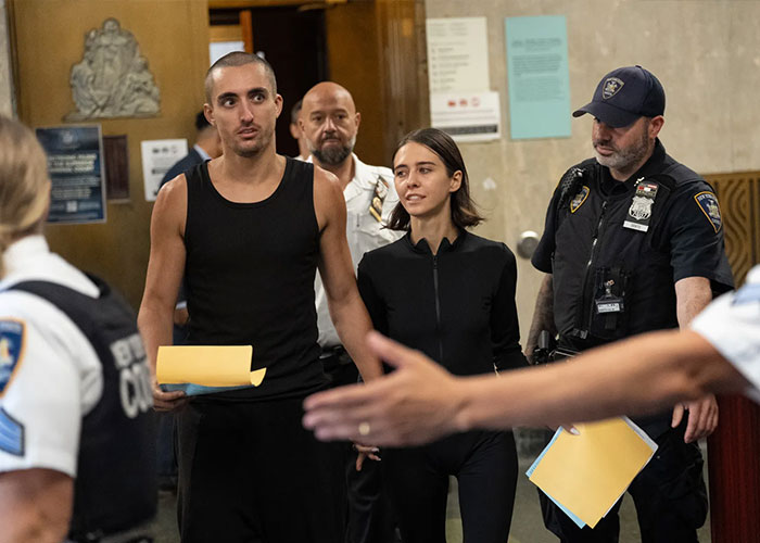 Two Empire State Building daredevils being led through a courthouse, followed by NYPD officers after their arrest.