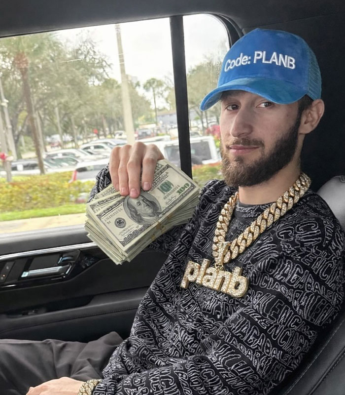 Man with a Plan B hat and chain holding money, connected to Bonnie Blue's baby shower scandal. Man with a Plan B hat and chain holding money, connected to Bonnie Blue's baby shower scandal.