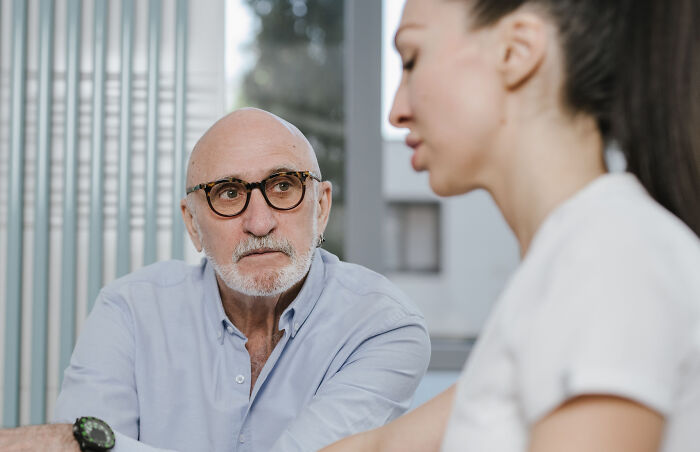 An older man with glasses talking to a younger woman, discussing age-gap relationships.