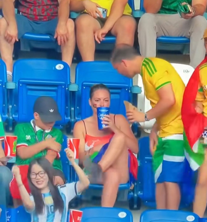 A woman sitting alone in the stands with her drink, after a viral World Cup moment backfire with her partner. A woman sitting alone in the stands with her drink, after a viral World Cup moment backfire with her partner.