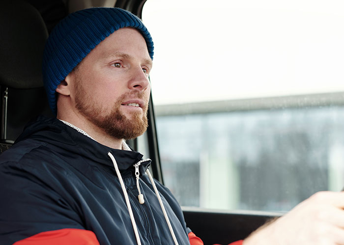 A man in a blue hat driving, focused, wondering about instances of reality break.