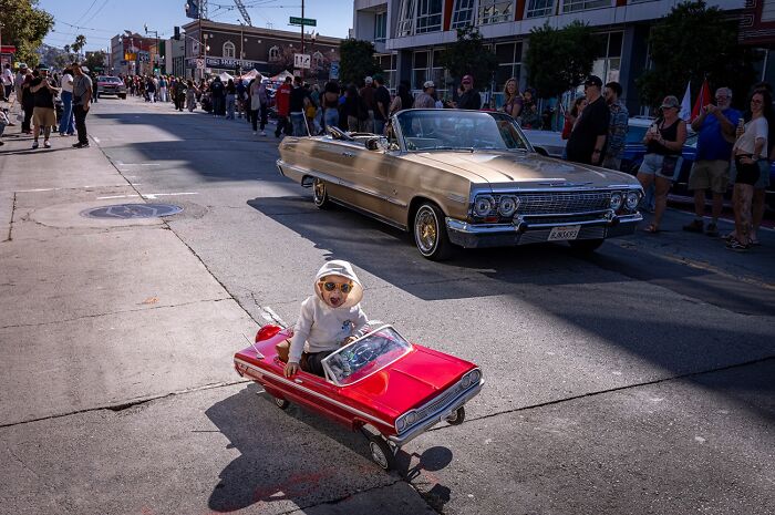 Photographer captures humor and chaos: a child in a toy car next to a classic convertible.