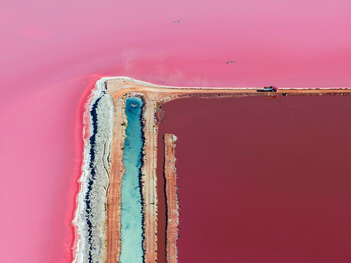 Aerial color photo of a vibrant pink and red lake with a thin blue channel, remarkably capturing the world.