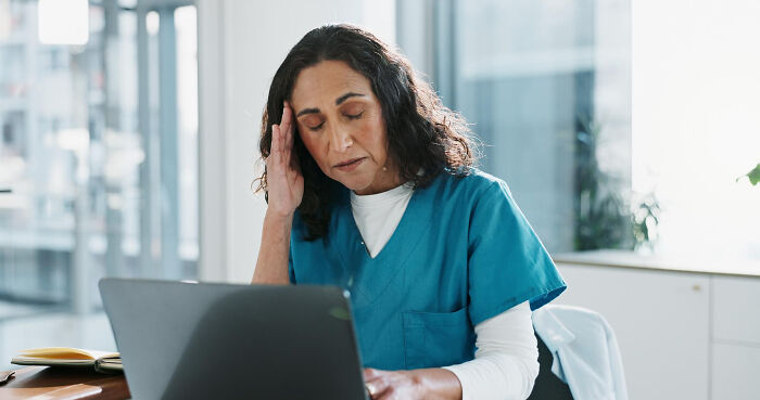 A female doctor in scrubs holds her head, showing the stress of the medical industry and healthcare truths.