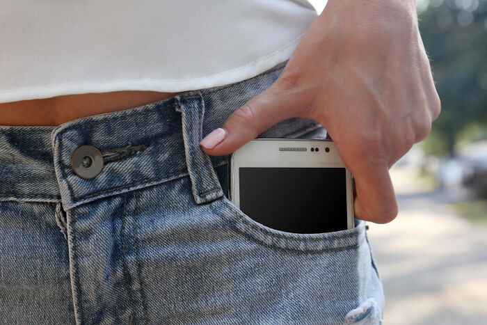A hand putting a phone into a jeans pocket, emphasizing the risk of pocket dial stories and the need to double-check your lock screen.