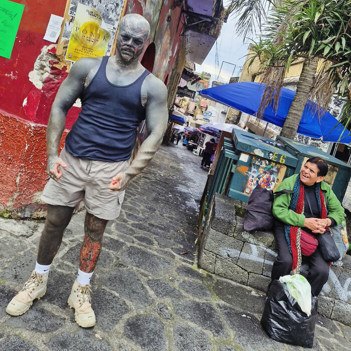 The Black Alien man stands on a cobblestone street, showcasing his body modifications and tattoos. The Black Alien man stands on a cobblestone street, showcasing his body modifications and tattoos.
