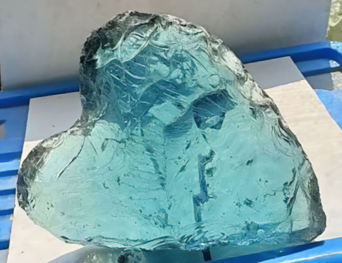 A large, irregularly shaped blue-green glass object on a blue surface, found in the Mojave Desert. A large, irregularly shaped blue-green glass object on a blue surface, found in the Mojave Desert.