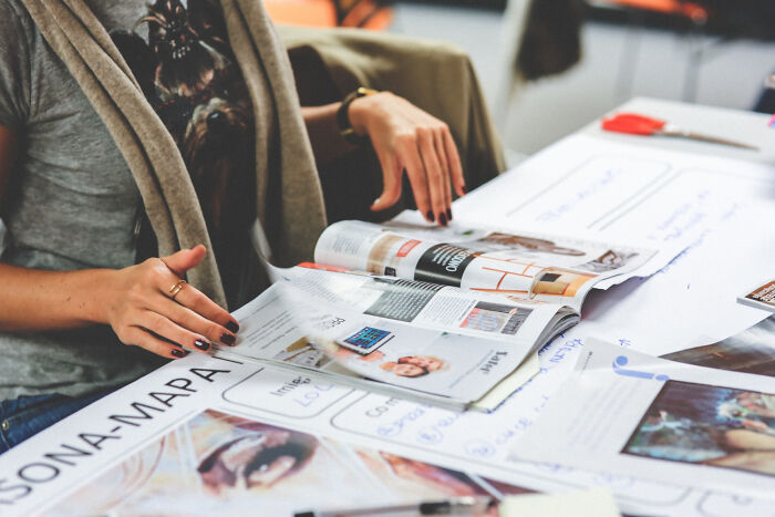 A female worker's hands flipping through a magazine, amidst papers related to corporate practices.