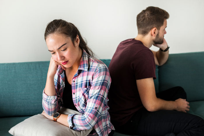 A couple sitting on a couch, backs turned to each other, illustrating the impact of an autism diagnosis on their relationship and family planning. A couple sitting on a couch, backs turned to each other, illustrating the impact of an autism diagnosis on their relationship and family planning.