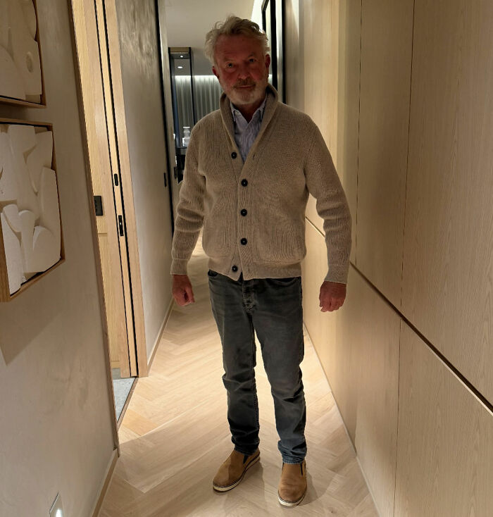 Sam Neill stands in a hallway, dressed in a casual cardigan and jeans, reflecting on Alec Baldwin's tribute. Sam Neill stands in a hallway, dressed in a casual cardigan and jeans, reflecting on Alec Baldwin's tribute.