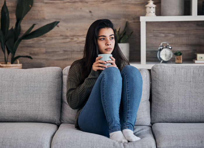 A thoughtful young woman holding a mug, contemplating the complex family dynamics of a delulu mom.