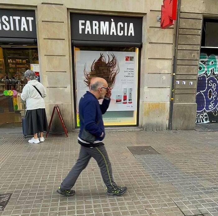 Perfectly timed coincidences in Barcelona: a bald man walks past a pharmacy advertisement for hair products.