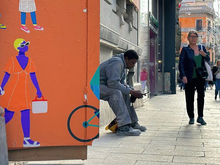 Perfectly timed coincidences in Barcelona: a man sitting beside a colorful mural depicting a person on a bicycle.